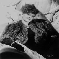 Bette Davis, позиращ с ръка в скута в черно козина и черна рокля с черни ръкавици